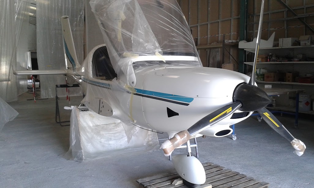 Un petit avion est stationné dans un hangar, avec divers outils et équipements aéronautiques visibles en arrière-plan.