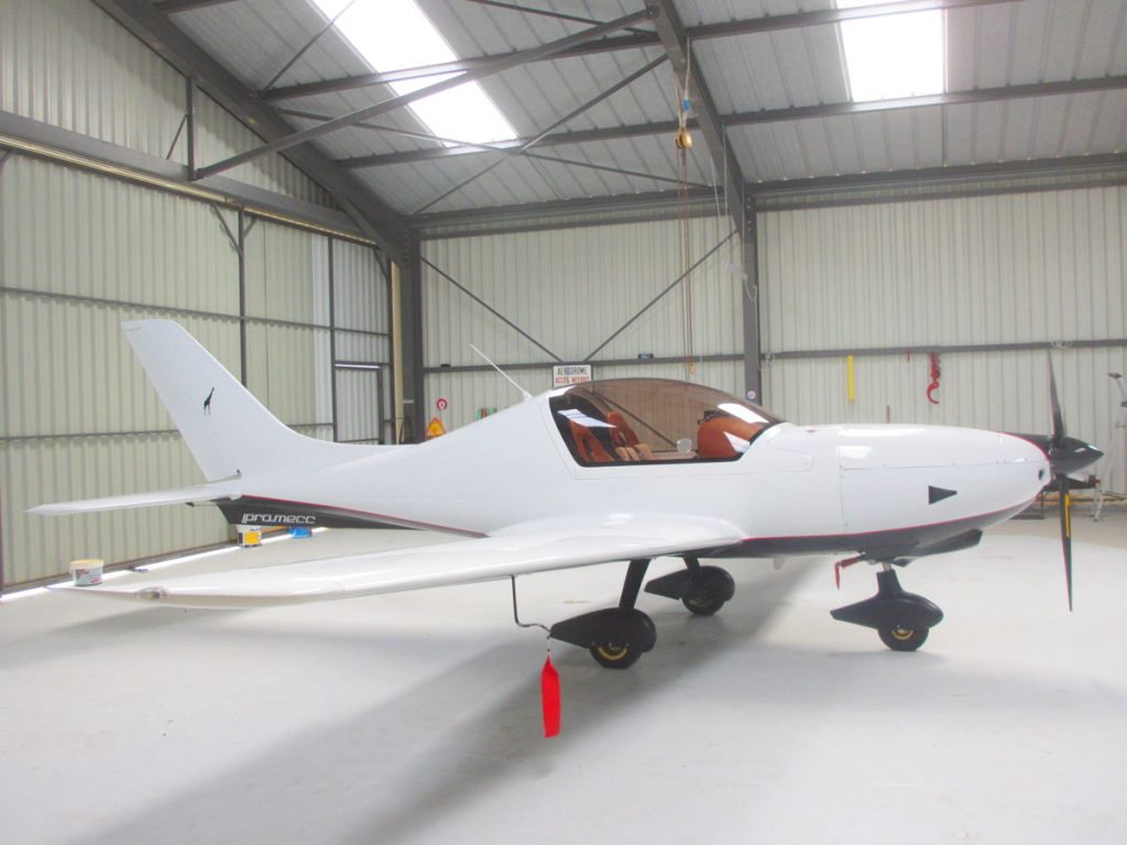 Un petit avion est stationné à l'intérieur d'un hangar, entouré d'outils et d'équipements de maintenance.