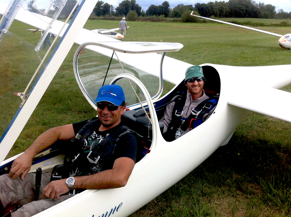Un petit avion est immobile dans un hangar, ailes repliées et porte du hangar entrouverte.